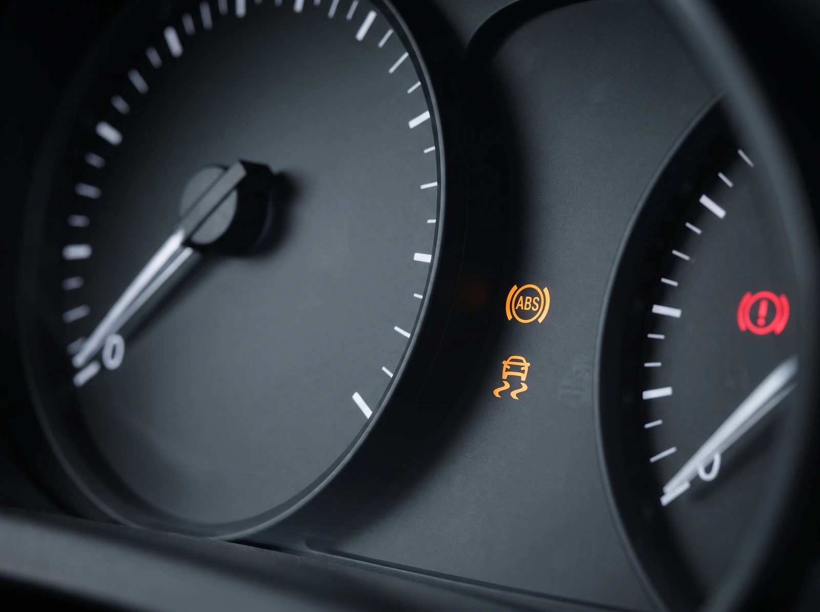 Instrument cluster macro shot showing the ABS warning lamp and traction control lamp lit together with the red brake warning lamp, speedometer needle at zero