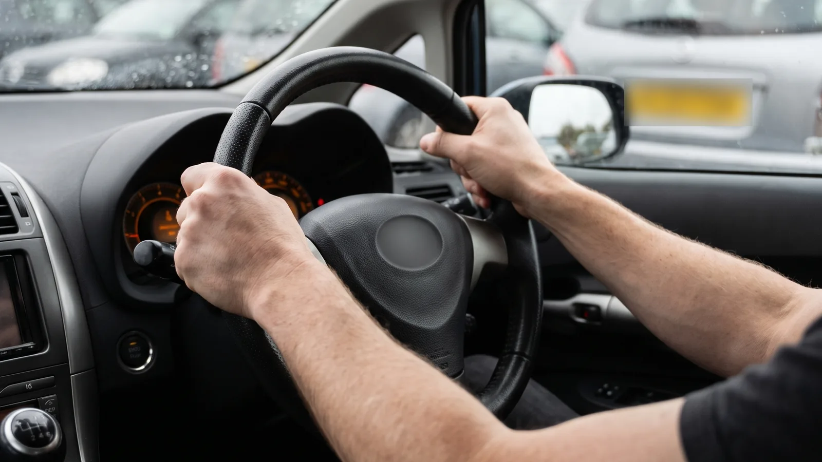 Driver's hands gripping the steering wheel of a right-hand-drive car in a UK car park, straining against heavy steering at low speed