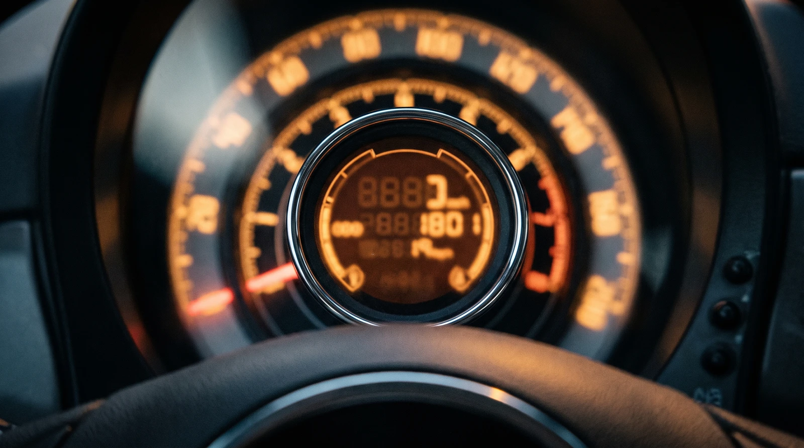 Fiat 500 instrument cluster close-up: the chrome-ringed central pod with its orange digital display, the mileage digits caught mid-flash, set inside the surrounding speedometer dial