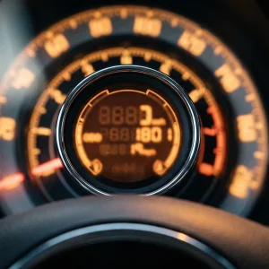 Fiat 500 instrument cluster close-up: the chrome-ringed central pod with its orange digital display, the mileage digits caught mid-flash, set inside the surrounding speedometer dial